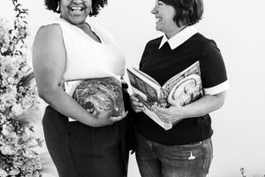 Two people stand together smiling and holding books while engaged in animated conversation.
