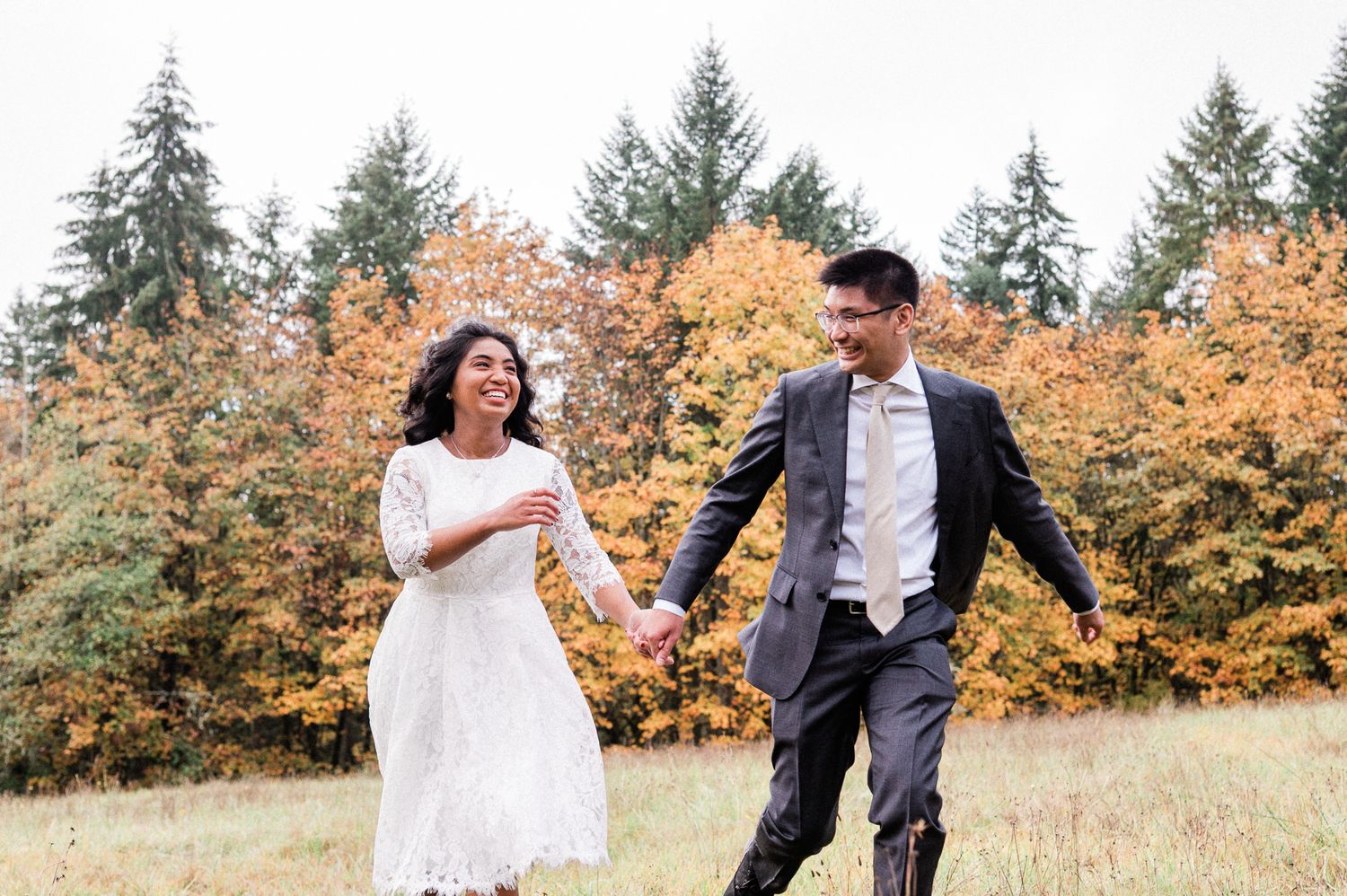 Couple walking through an autumn meadow with golden foliage and evergreen trees in the background