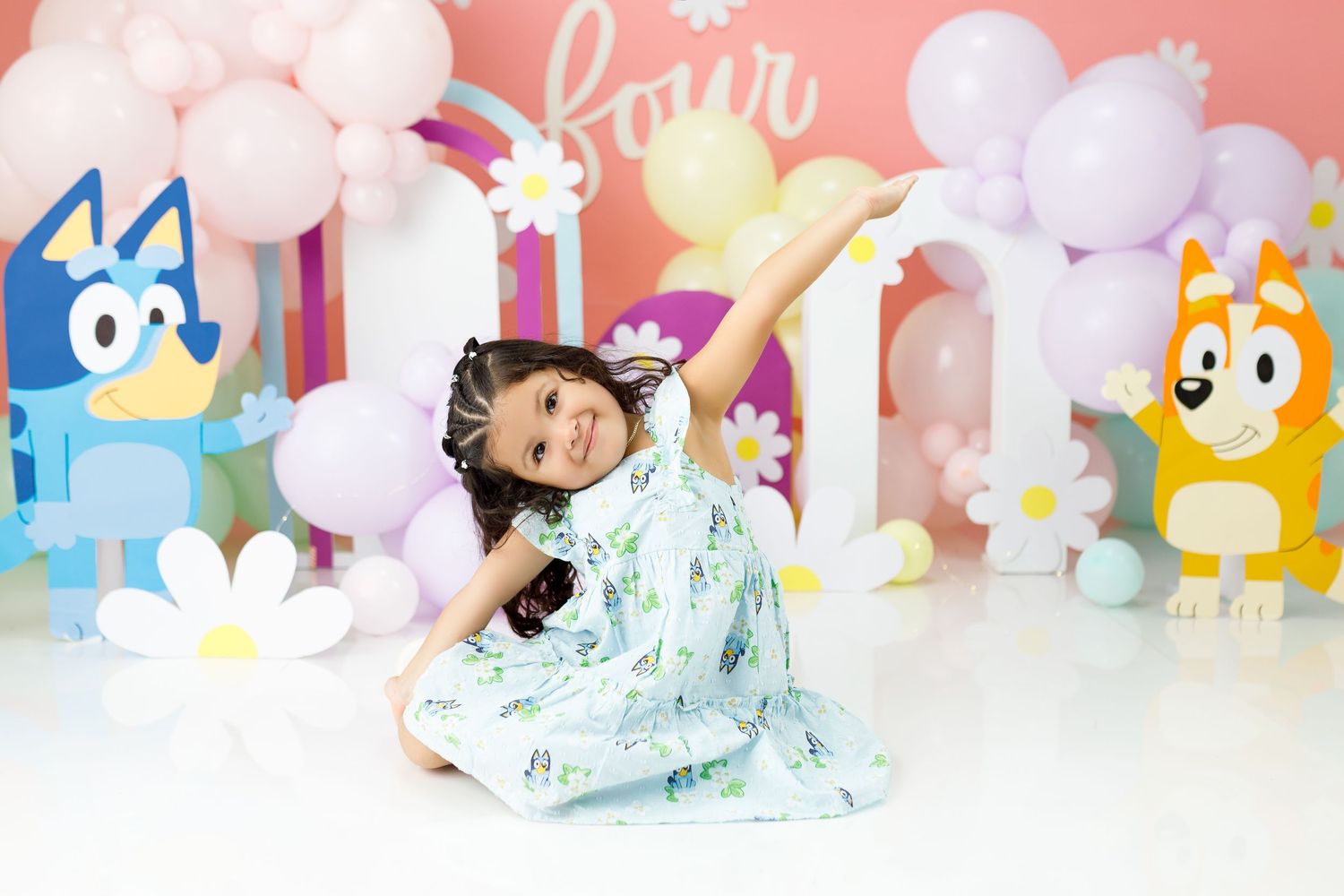 Colorful pastel party decorations with balloons, stuffed animals, and soft toys arranged against a pink backdrop.