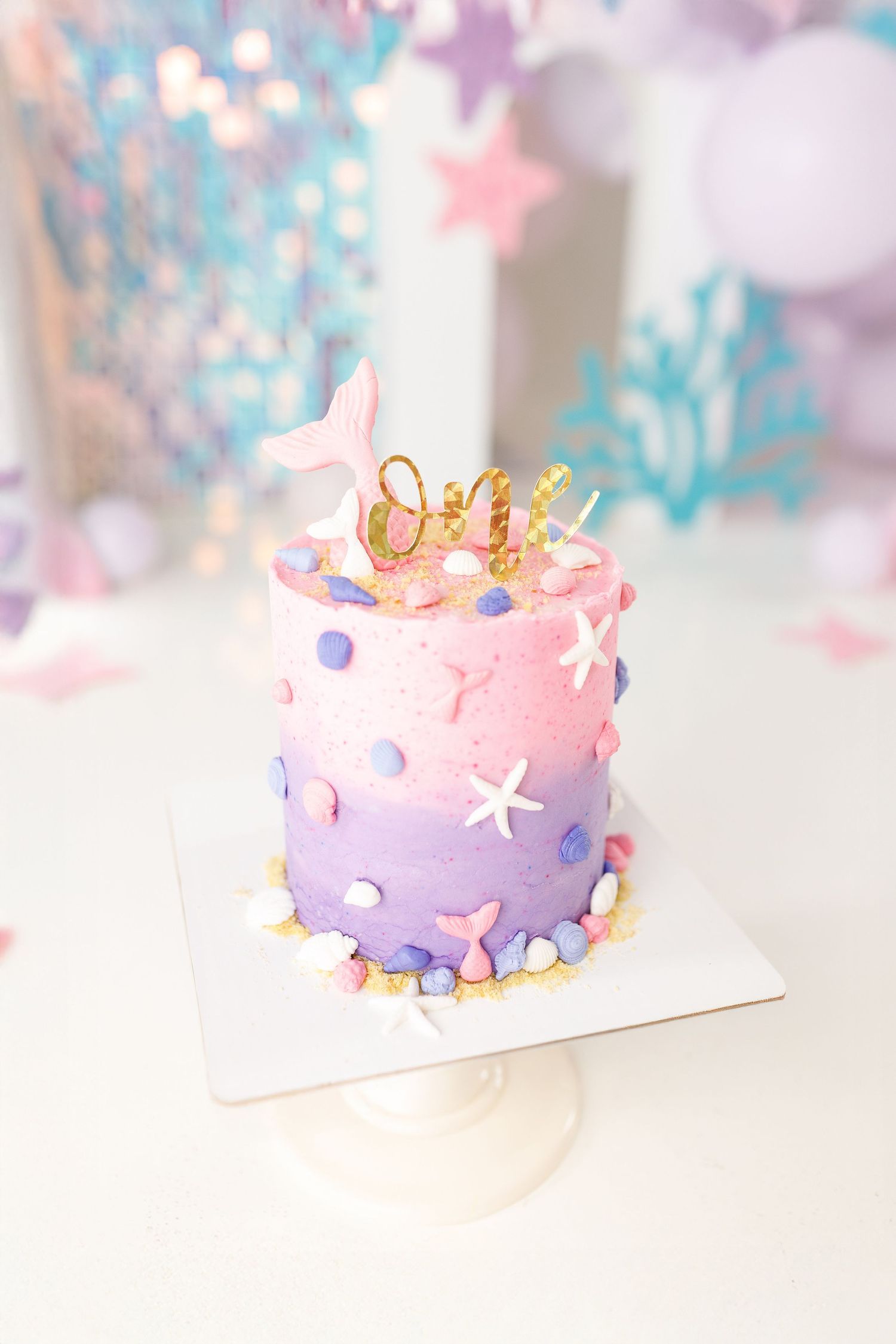 A pastel purple and pink birthday cake decorated with gold accents and colorful polka dots on a white surface.