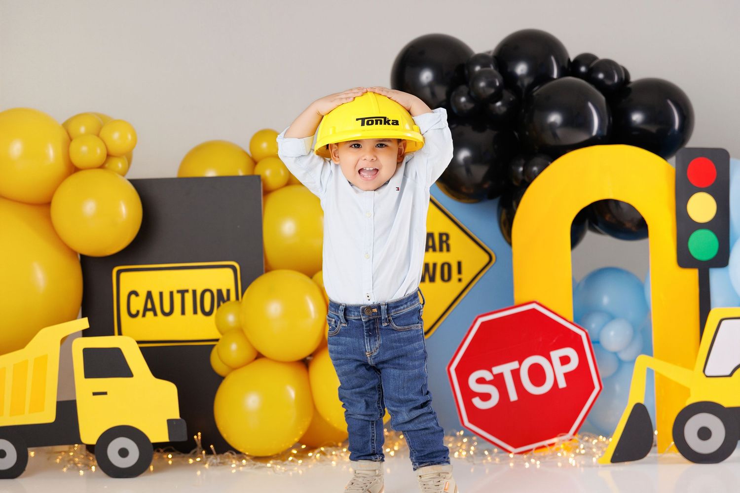 Construction themed birthday party setup with yellow and black balloons, toy trucks, traffic signs and safety decorations.