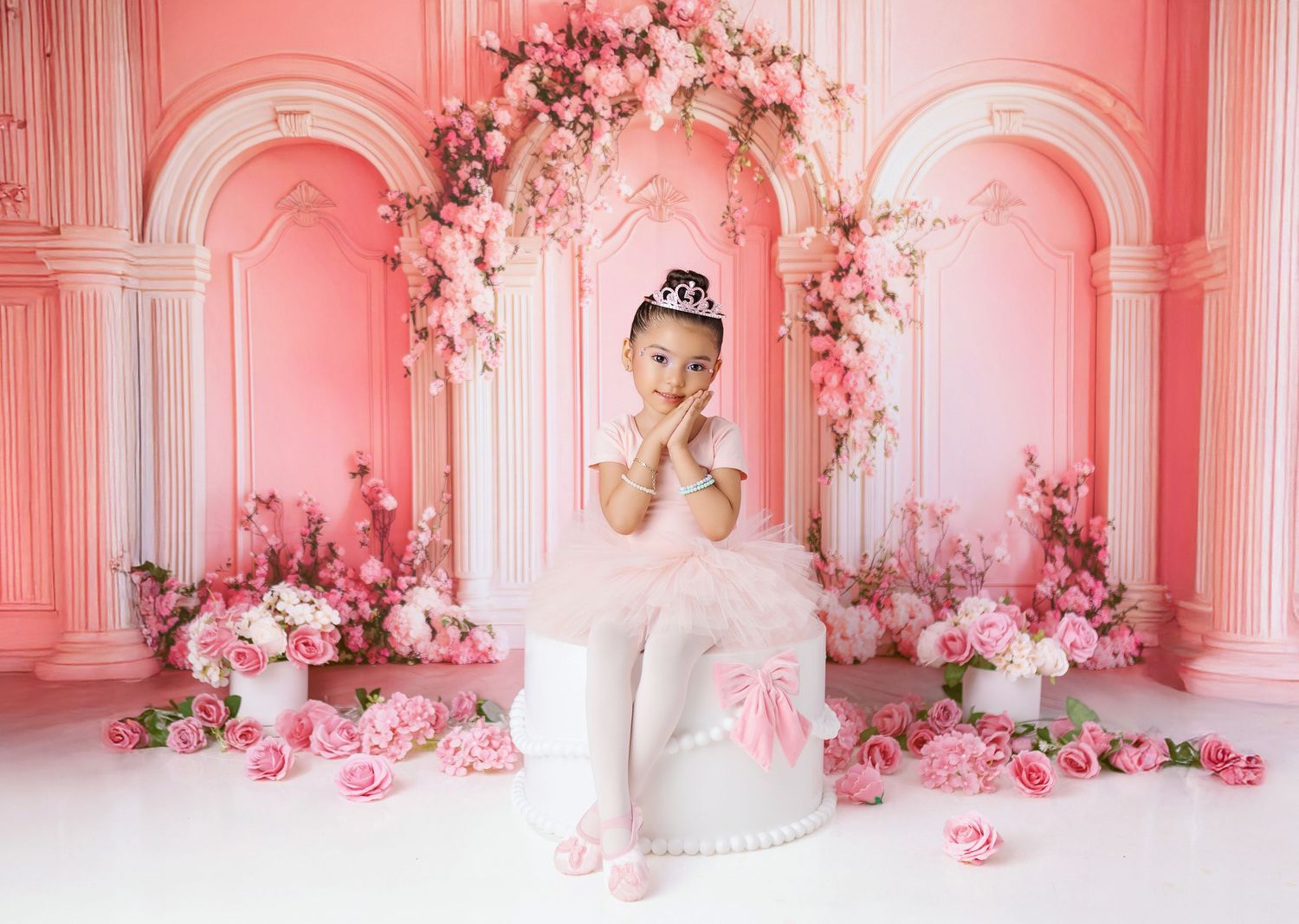 Elegant ballet dancer in white tutu poses in pink archway decorated with romantic floral arrangements and roses.