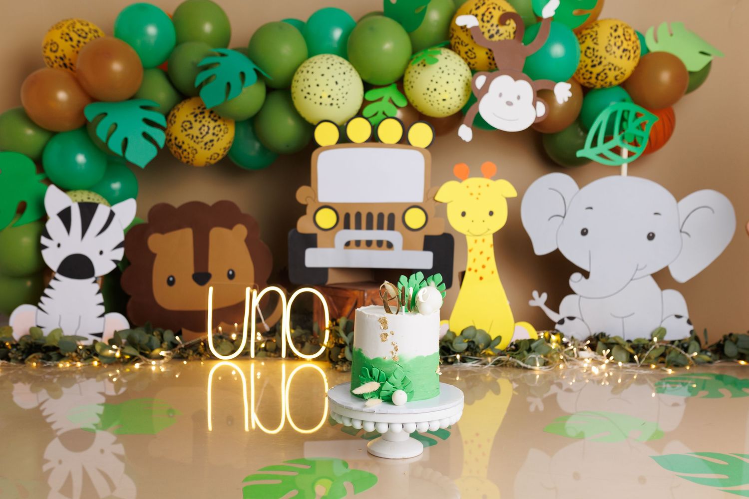 Safari themed birthday party setup with balloon arch, jungle animal cutouts and a yellow uno sign against a green backdrop.