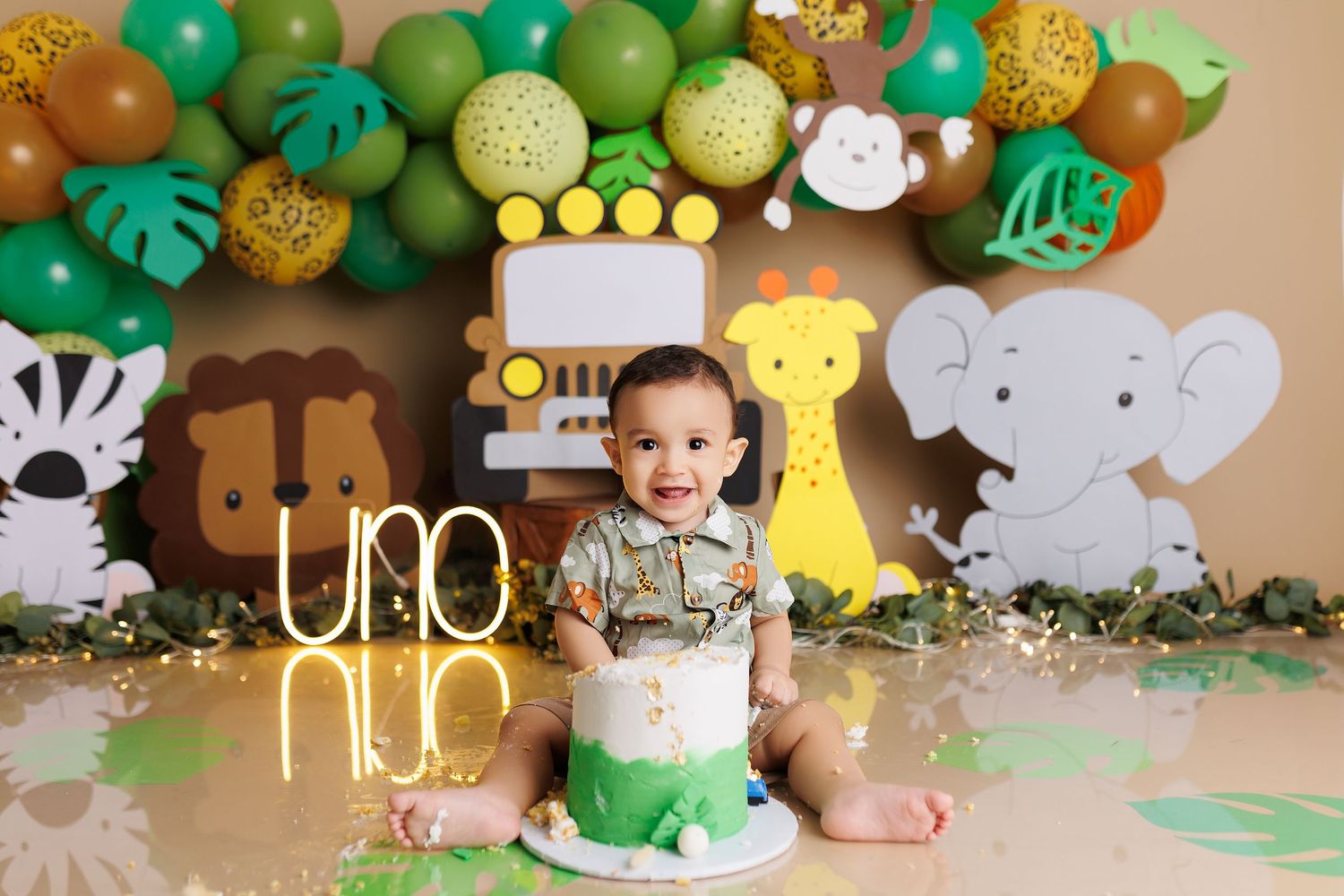Safari-themed first birthday party setup with green and gold balloons, animal cutouts, and jungle decorations.