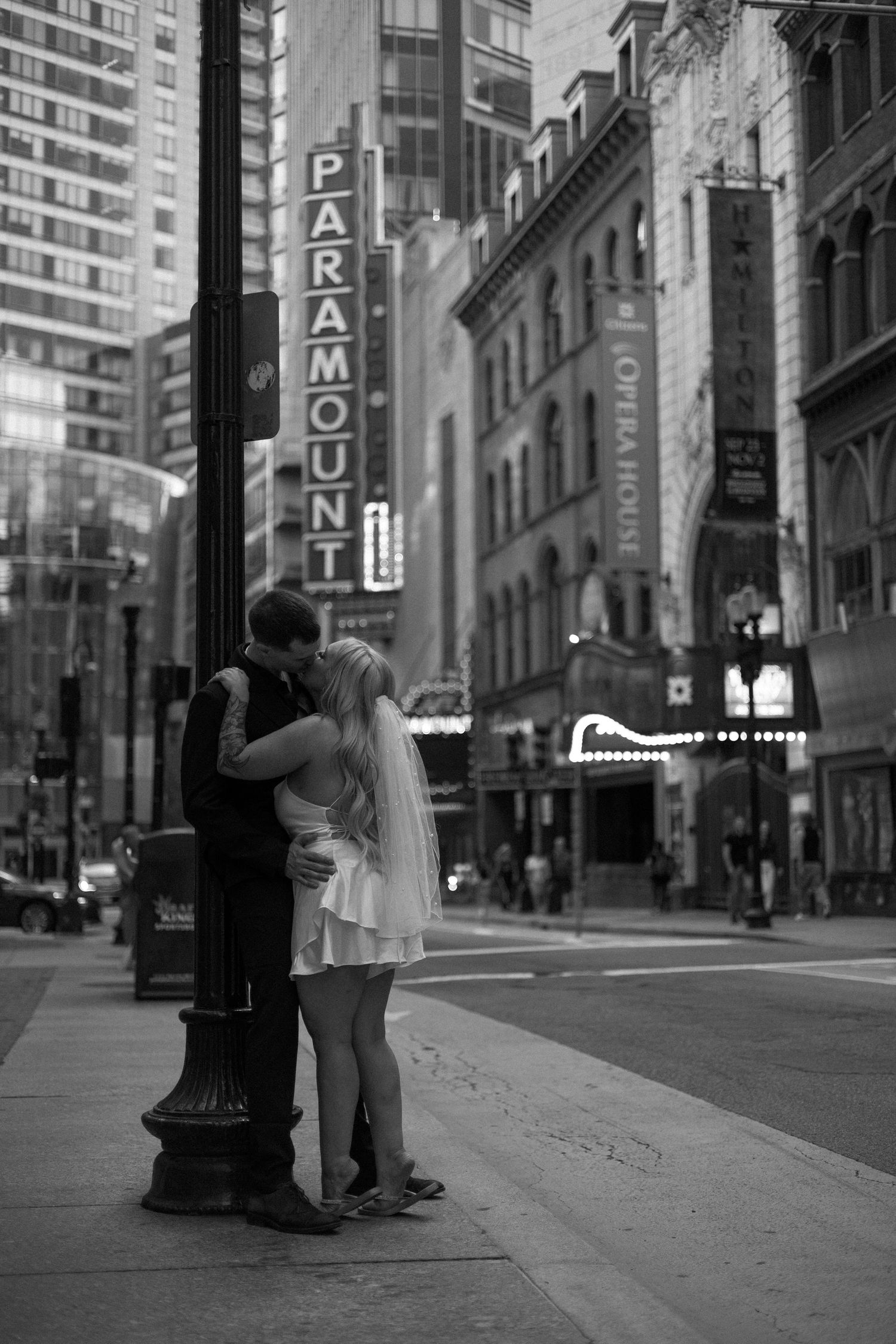 A series of black and white photos showing people embracing against a city street backdrop with tall buildings.