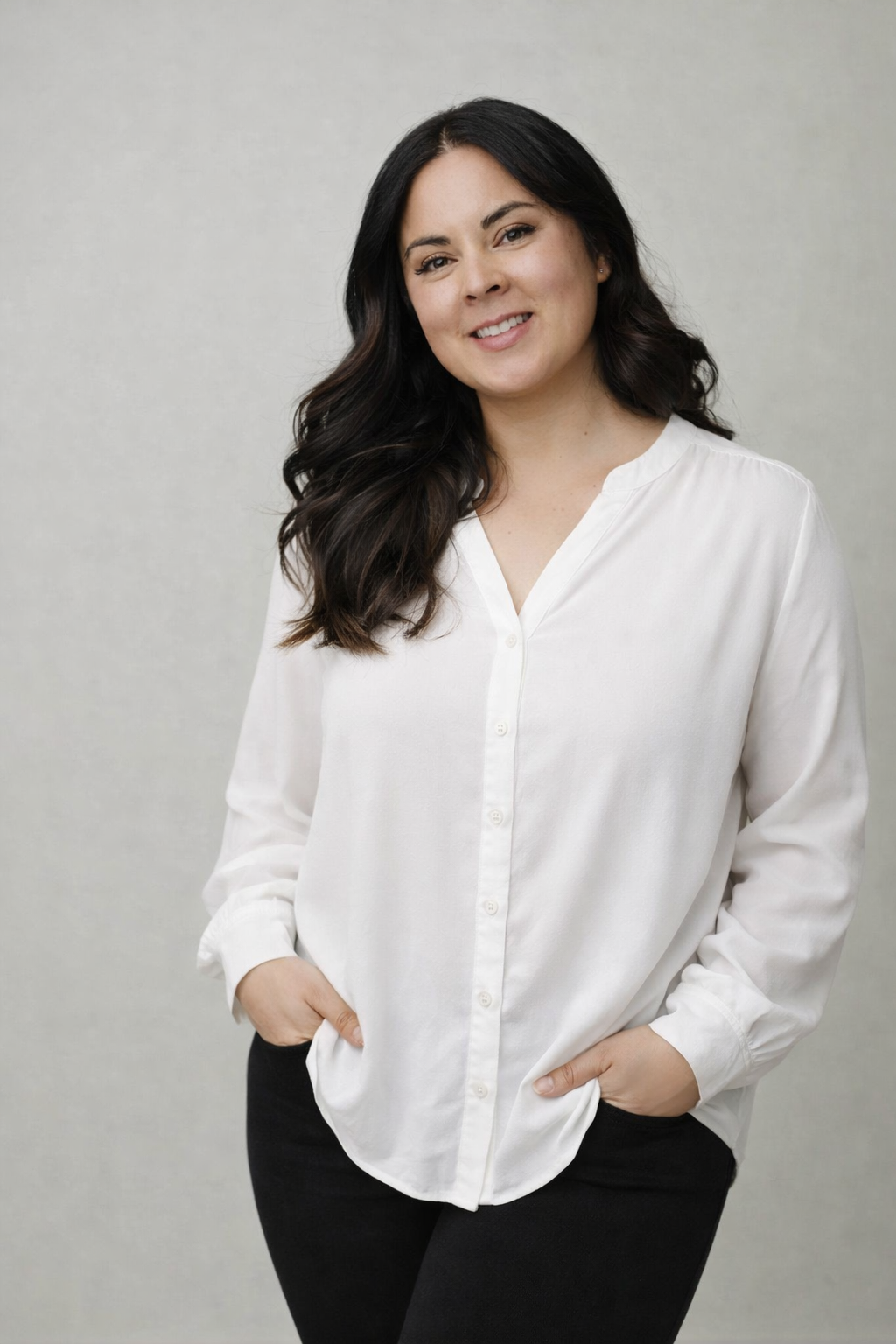 Professional studio portrait of a woman in a white button-down blouse and black pants against a light gray background. Elizabeth Lang Photo