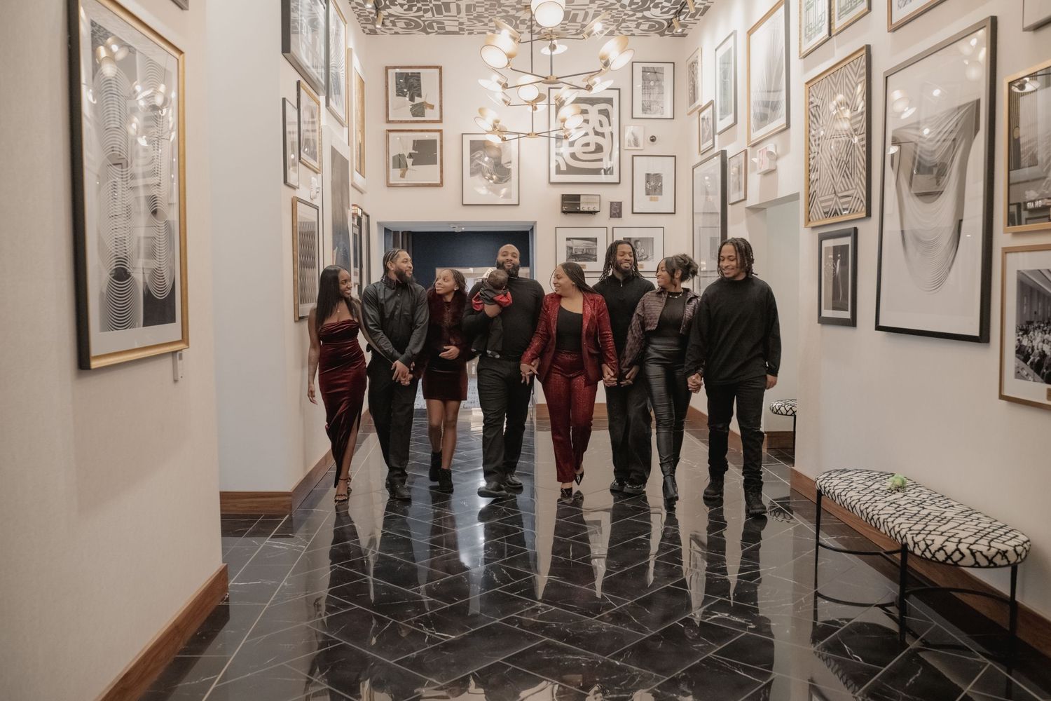 A group of visitors exploring an ornate gallery hallway with framed artwork on white walls and a decorative ceiling.