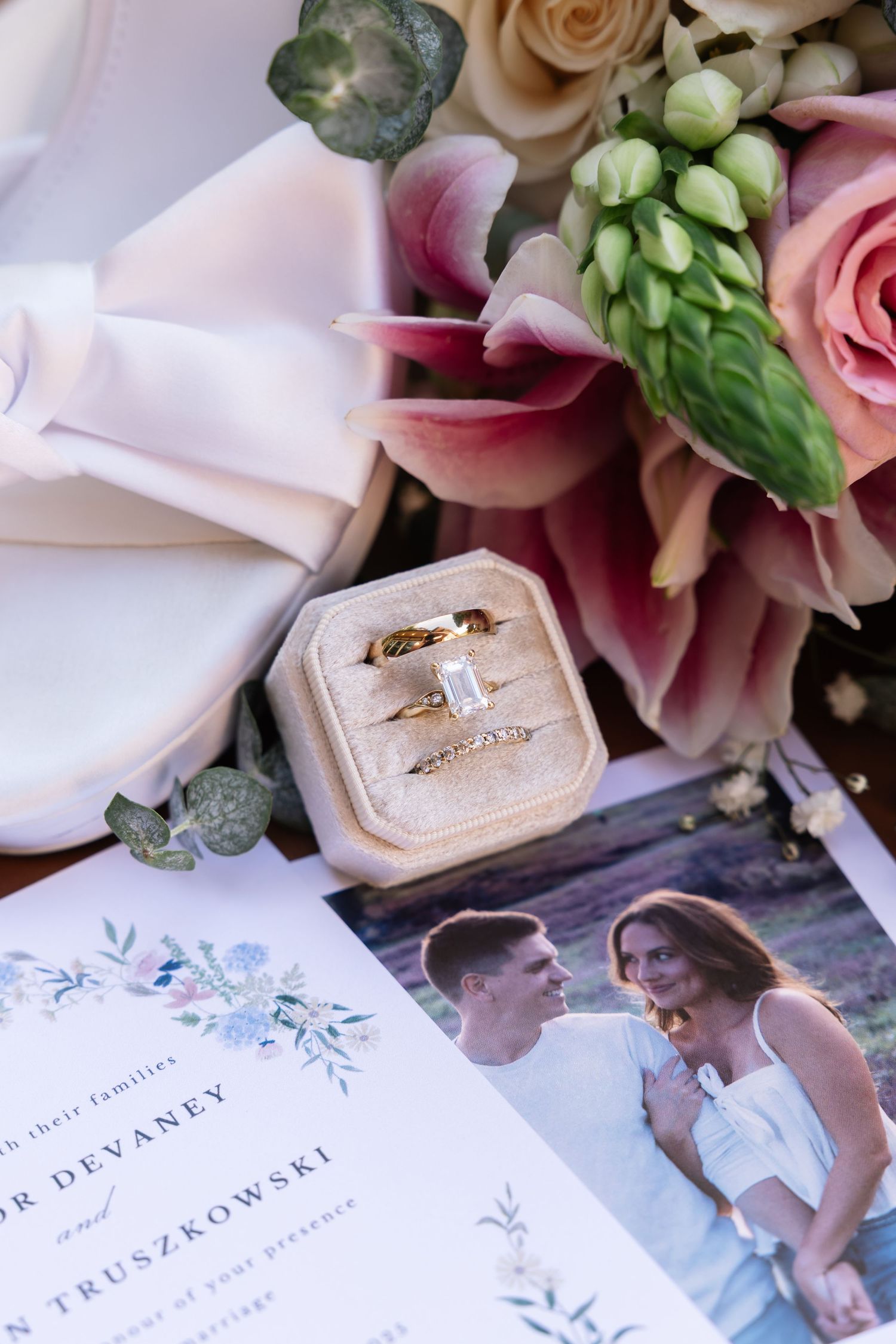 Wedding details featuring engagement rings in velvet boxes alongside floral arrangements and invitation cards with watercolor designs.