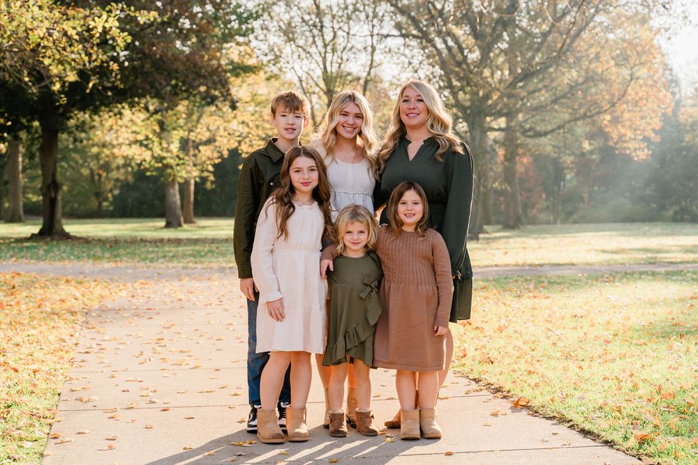 Group poses together on fallen autumn leaves in a sunlit park during golden hour.