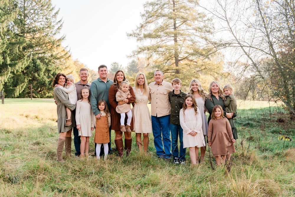 A group poses together outdoors in coordinated neutral-toned outfits against a natural landscape setting.