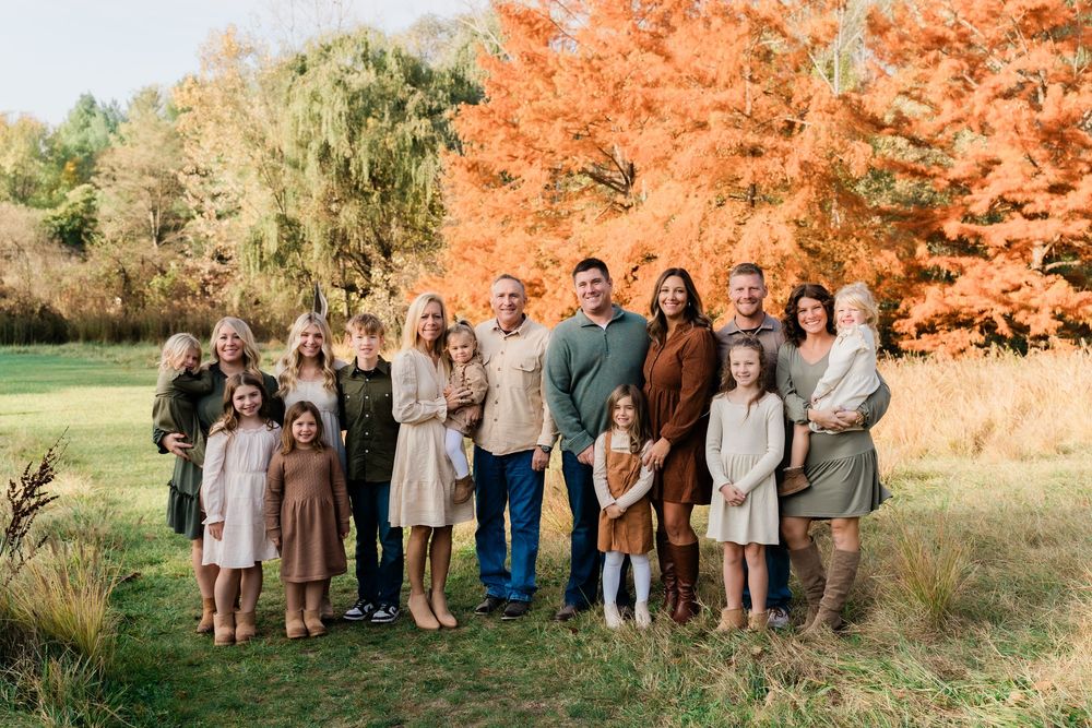 A group poses together outdoors against vibrant orange autumn foliage in a natural setting.