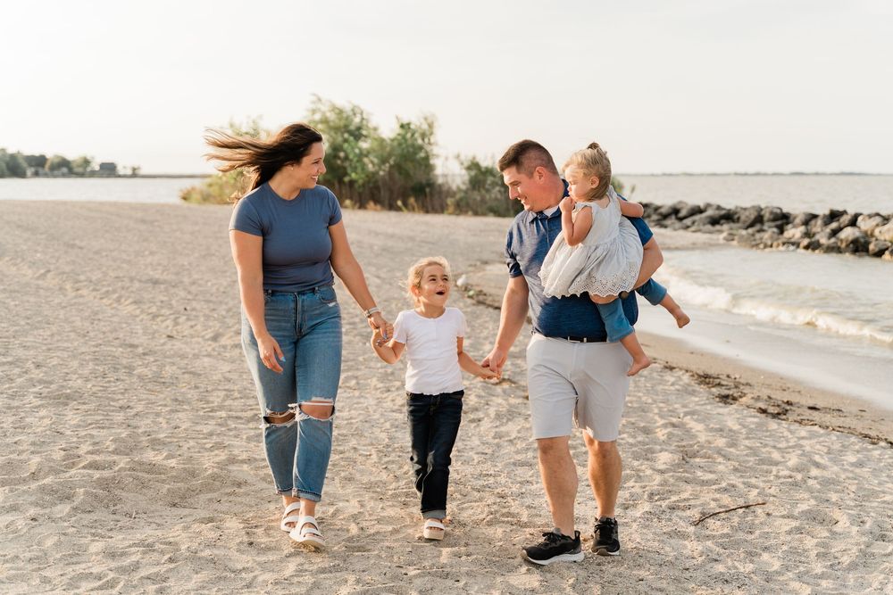 Family walking and playing together on a sandy beach at sunset with ocean waves in the background.