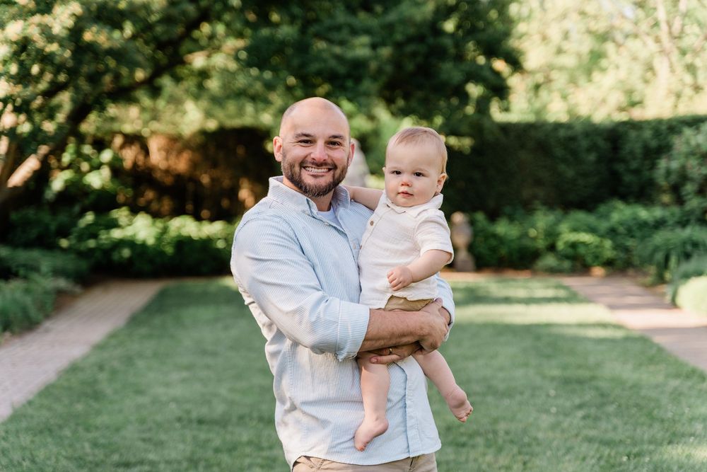 A parent and baby enjoy a playful moment together in a sunny garden setting with lush green grass.
