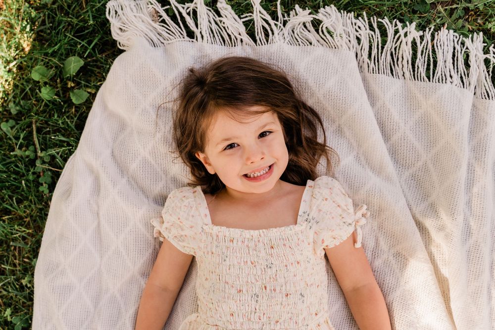 A child in a delicate lace dress poses against a white macrame backdrop in natural outdoor lighting.