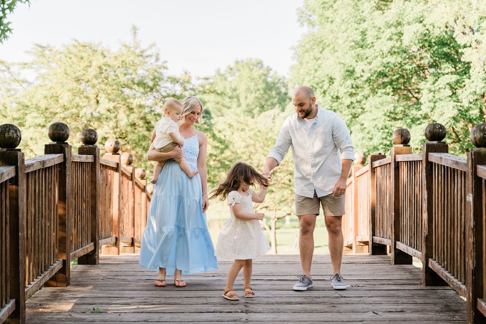 A couple dances together on a rustic wooden bridge surrounded by lush greenery on a sunny day.
