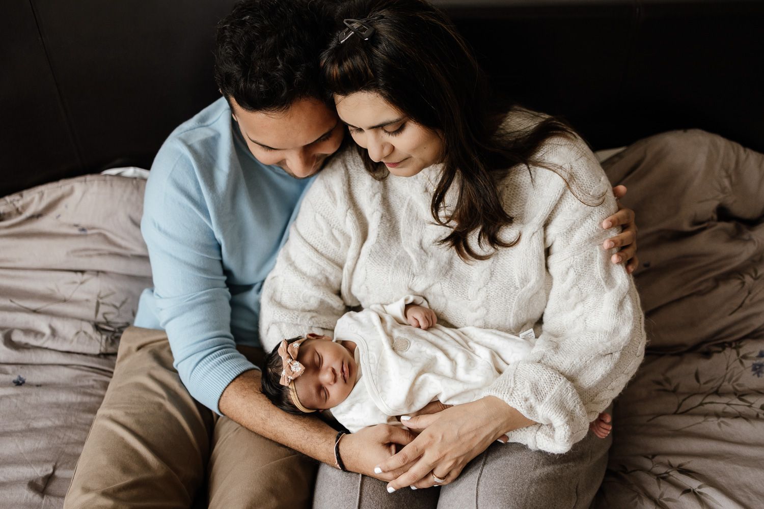 Parents cuddle their newborn baby at their in-home newborn photoshoot in San Jose