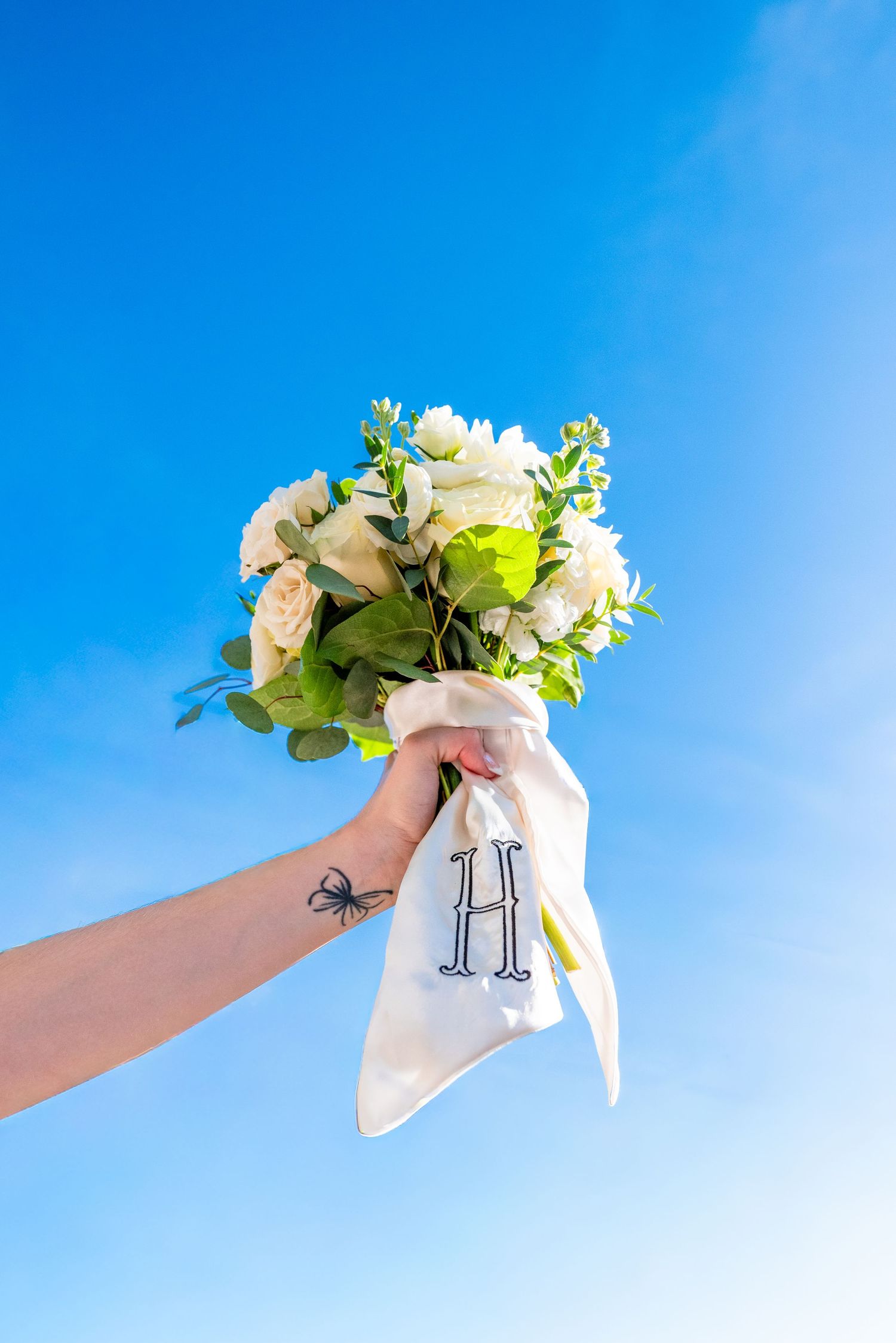 A delicate floral bouquet held against a bright blue sky with white flowers and greenery.