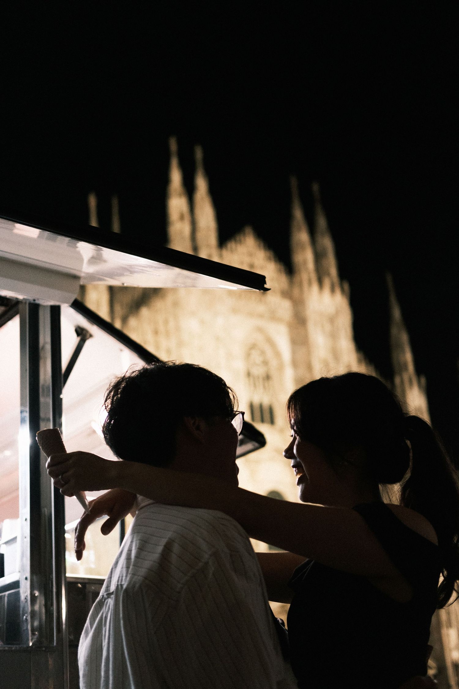 Silhouettes of two people looking out towards illuminated gothic cathedral spires at night.