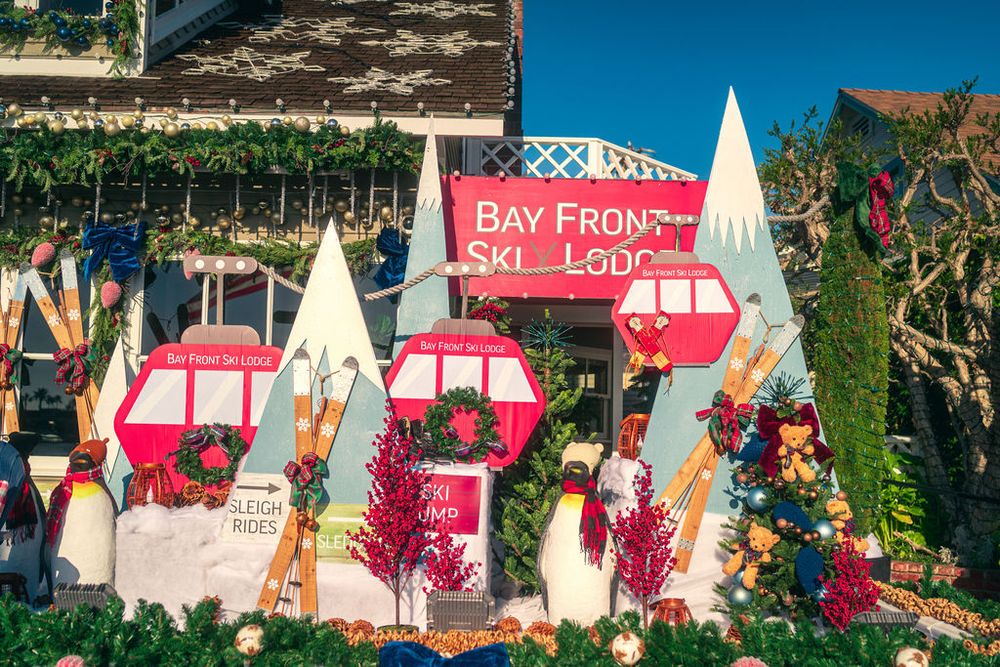 Colorful sailboats and nautical flags line a marina dock against a bright blue sky and waterfront buildings.