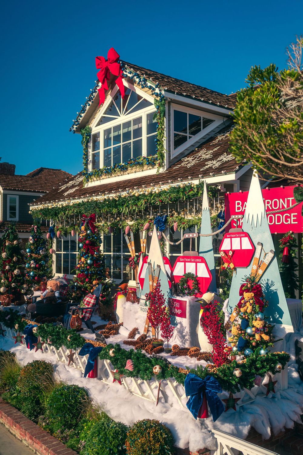 Holiday decorations and lights adorn a coastal lodge with red bows and white garlands against a bright blue sky.