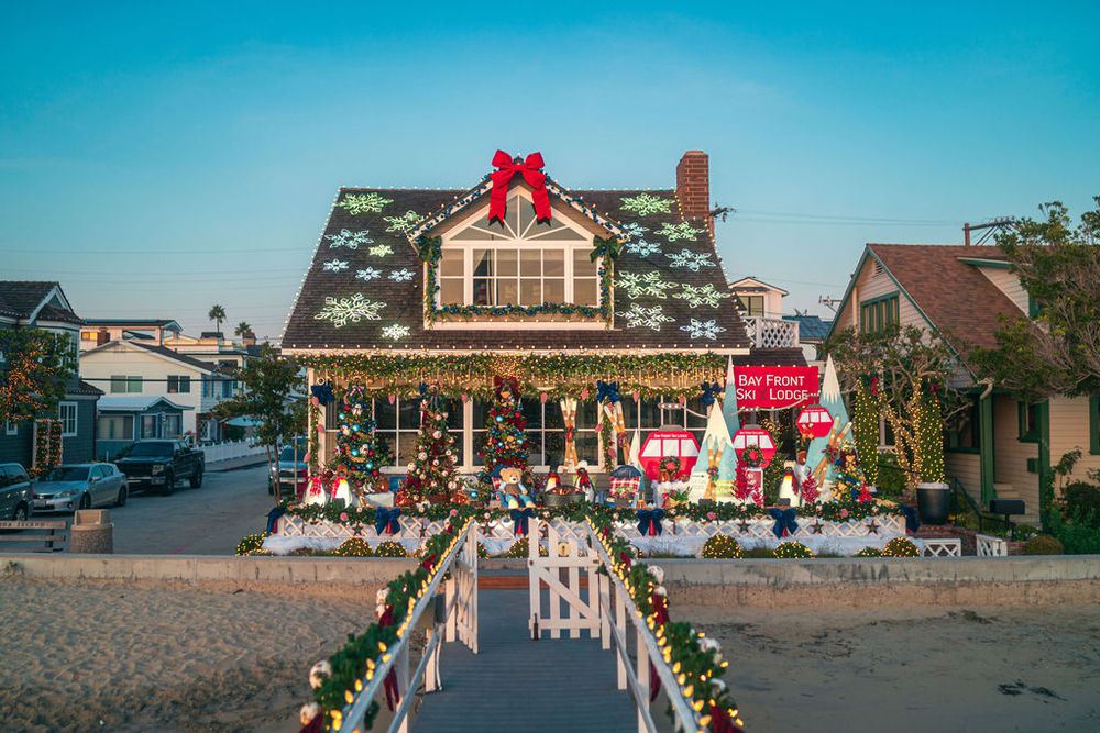 Row of seaside houses adorned with Christmas decorations and red bows along a sandy beach during daytime.