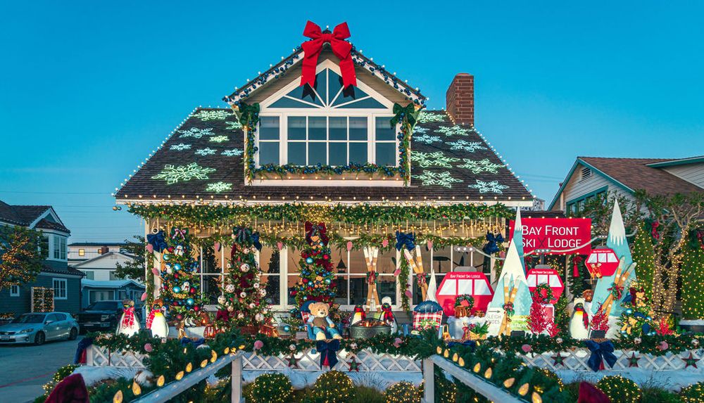 A series of coastal homes decorated with festive Christmas lights, garlands, and red bows along the waterfront.