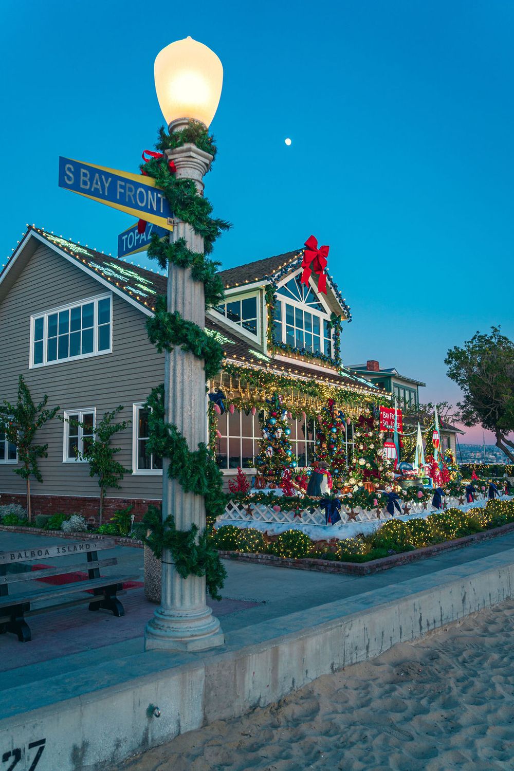 Christmas decorated storefront on Balboa Island with illuminated lamp post and garland along S Bay Front street at dusk.
