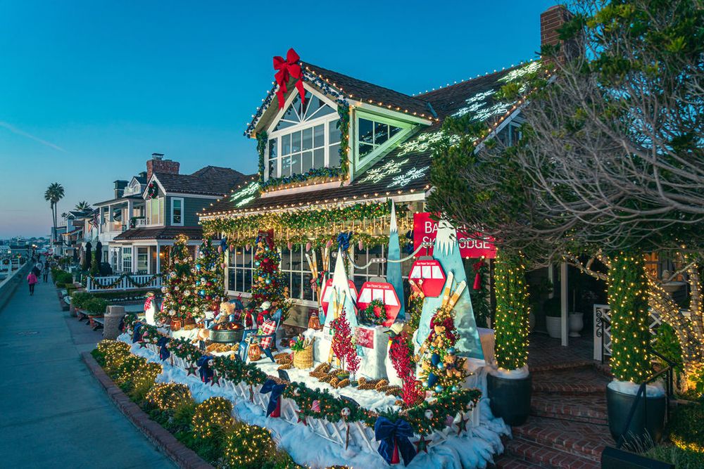 Festive Christmas decorations line the exterior of a waterfront lodge with twinkling lights and red accents.