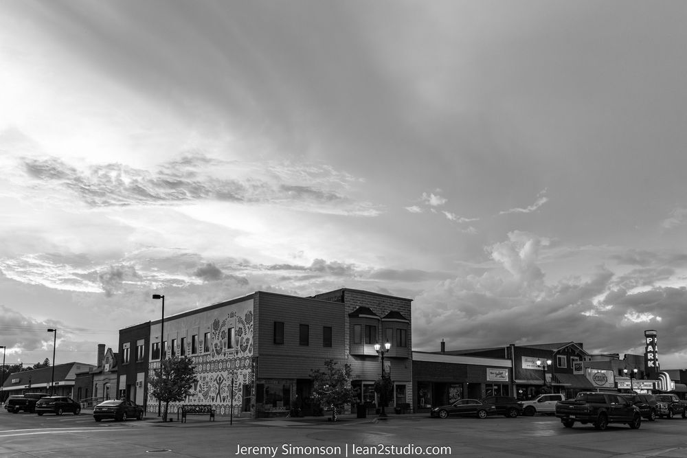 A panoramic black and white view of vintage storefronts and buildings along a small town main street.