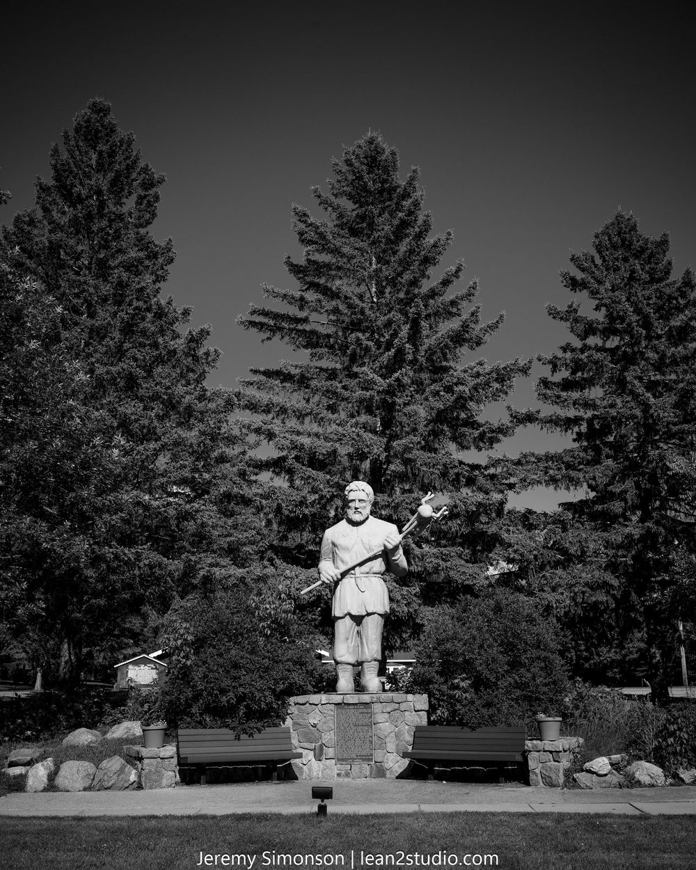 A black and white panoramic sequence showing a large white statue among tall pine trees against a dark sky.