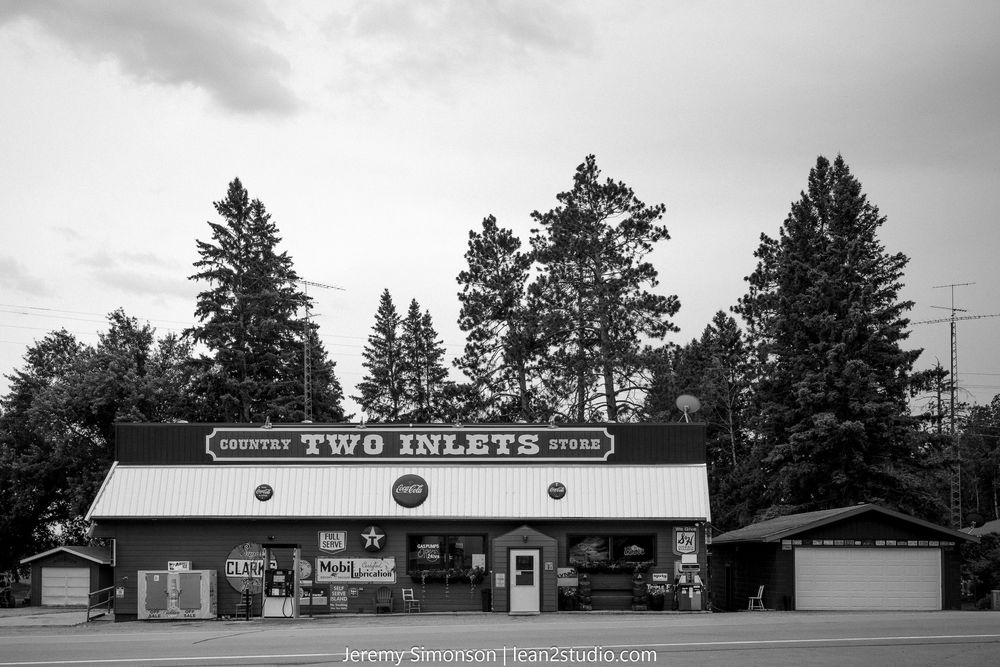 Black and white panoramic view of retro commercial buildings and gas stations along a rural highway.