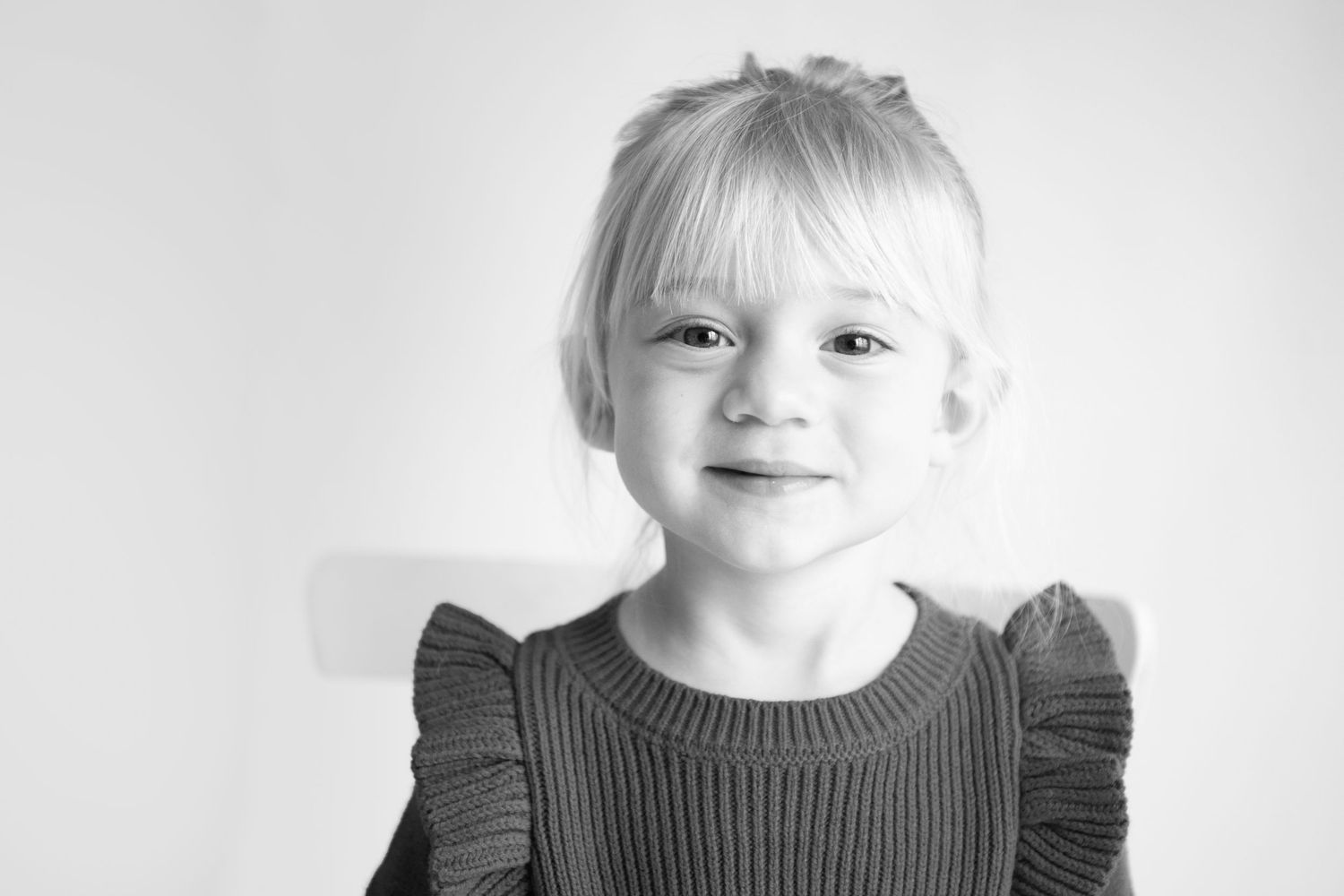 Black and white portrait of a young child wearing a ribbed sweater with ruffled shoulders.