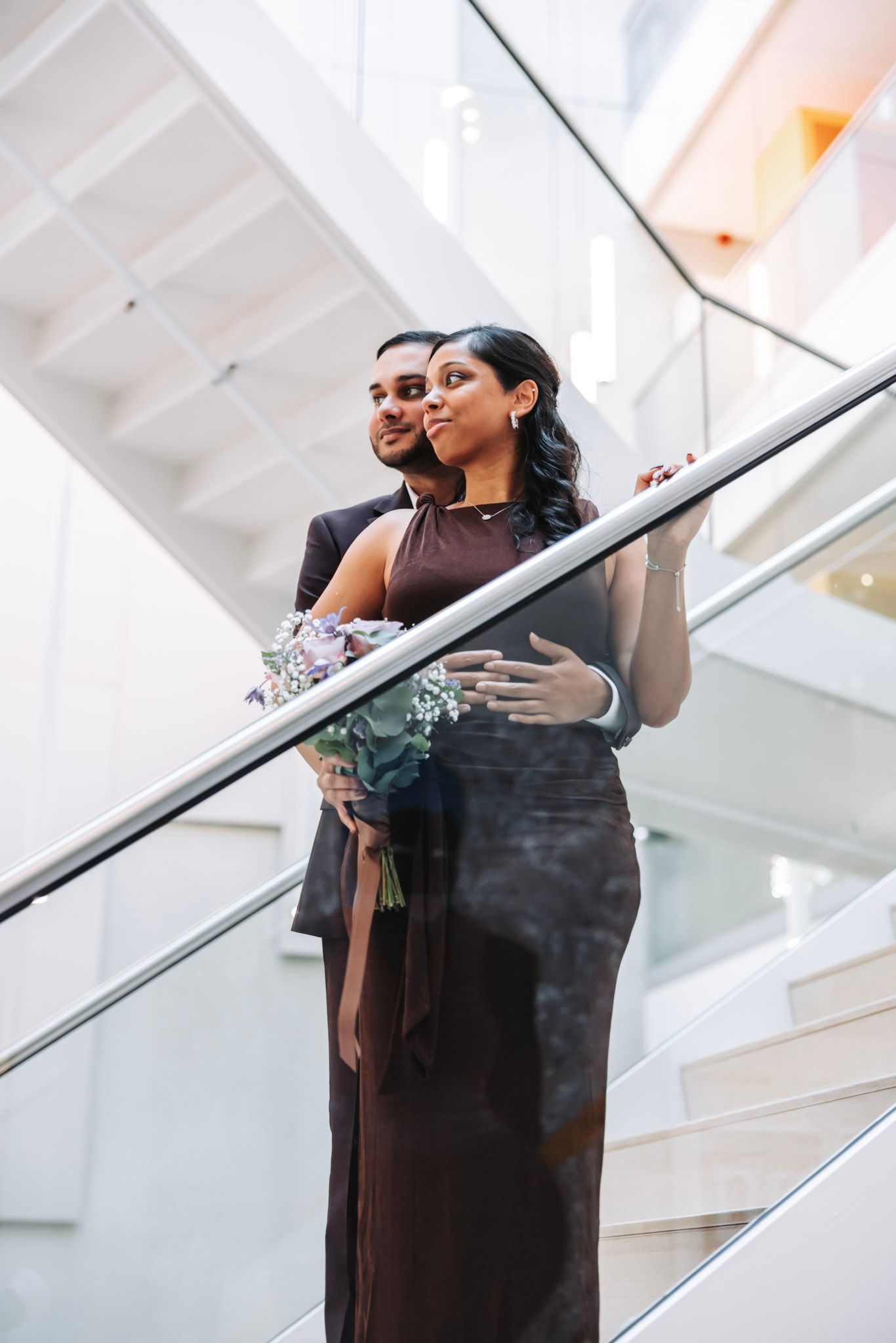 A couple in formal attire posing on the staircase in the bright atrium of Gemeente Hoofddorp Beukenorst