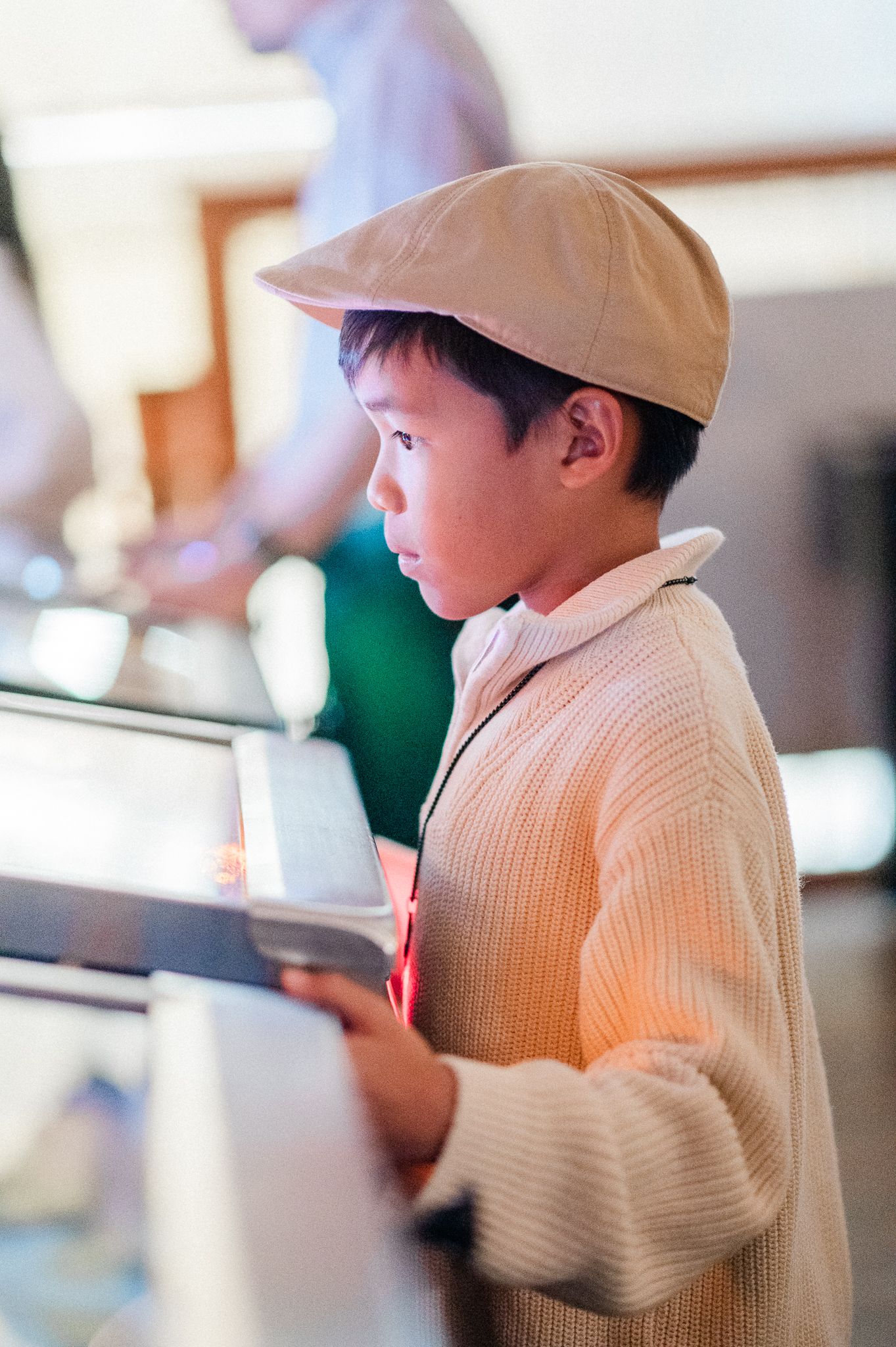Young child in beige sweater and baseball cap playing on a pinball machine