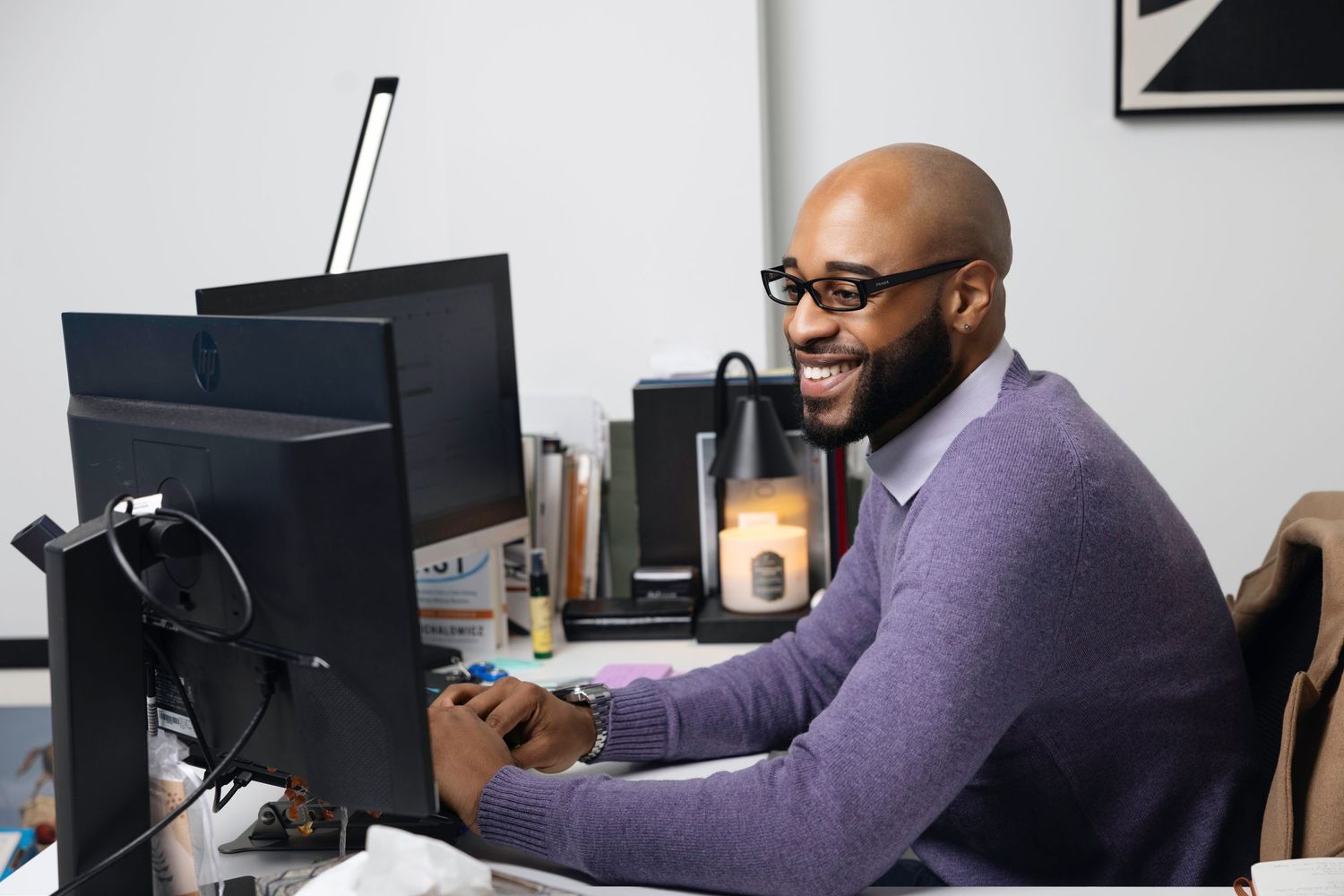 Professional working at computer desk in purple sweater in modern office environment.