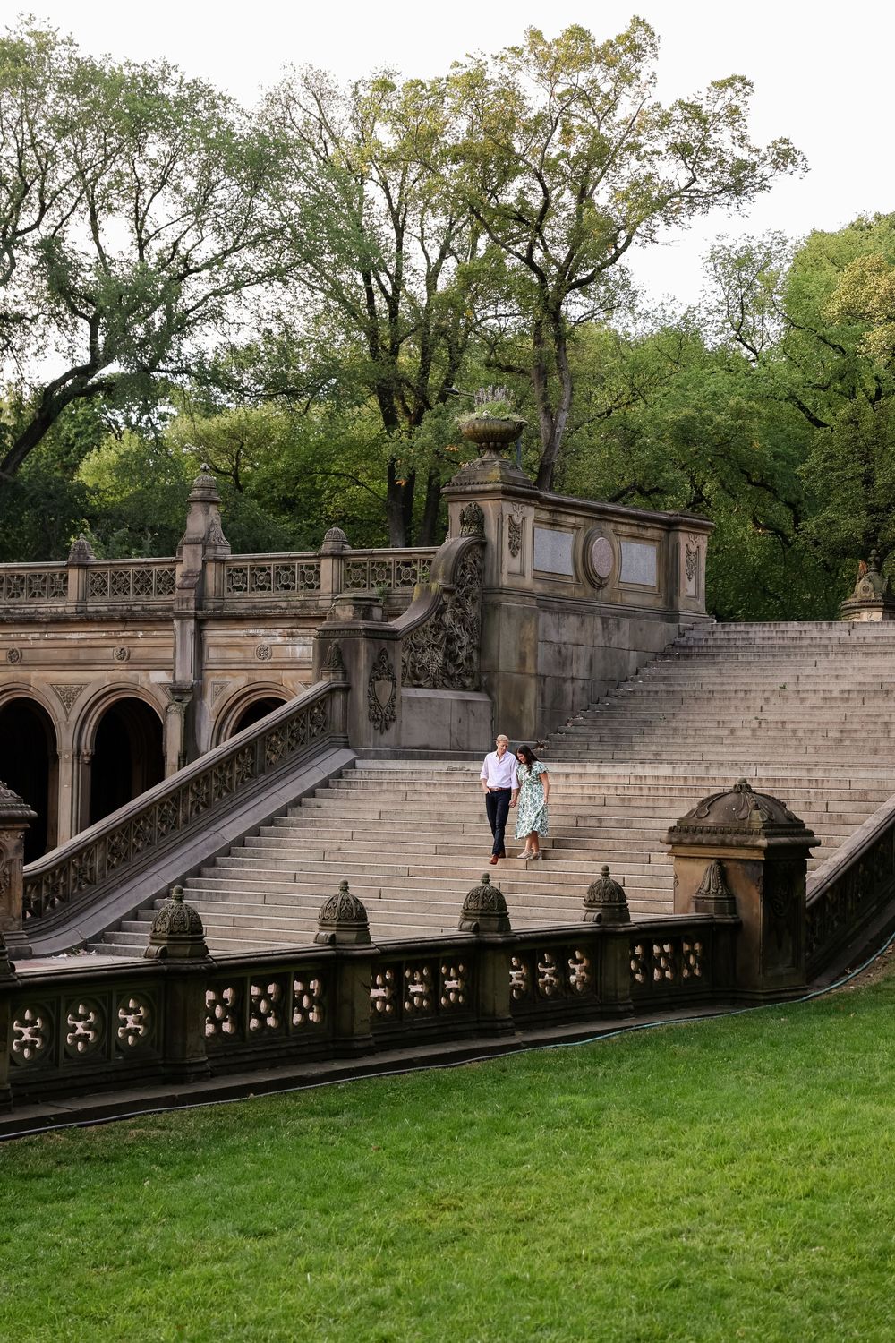 Historic stone staircase with ornate railings and archways in Central Park leads up a grassy hill on an autumn day.