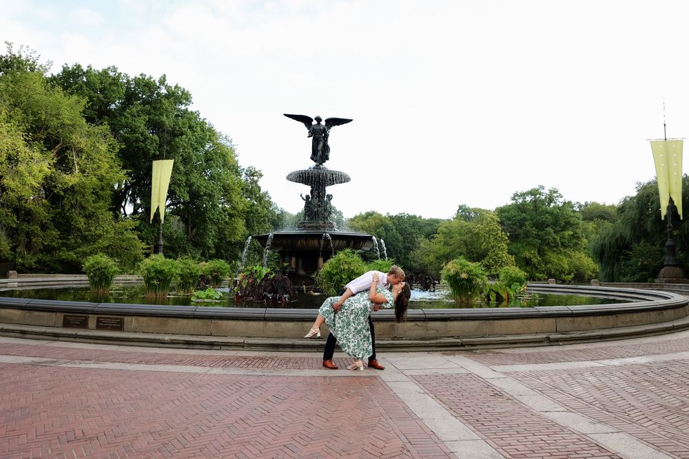 Panoramic view of Bethesda Fountain and Terrace in Central Park surrounded by lush green trees on a sunny day.