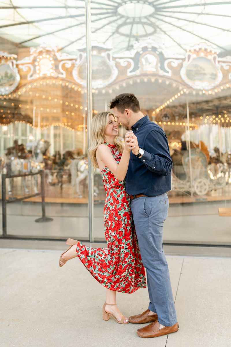 A couple embraces in a playful dance pose by an illuminated carousel display.