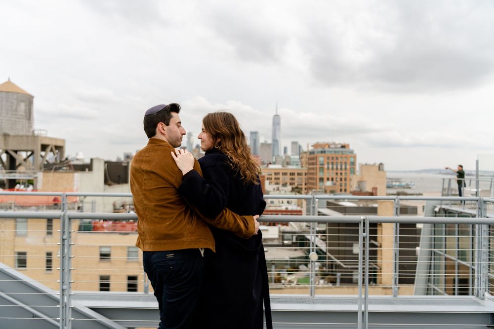 Romantic couple embracing on urban rooftop with Manhattan skyline views.