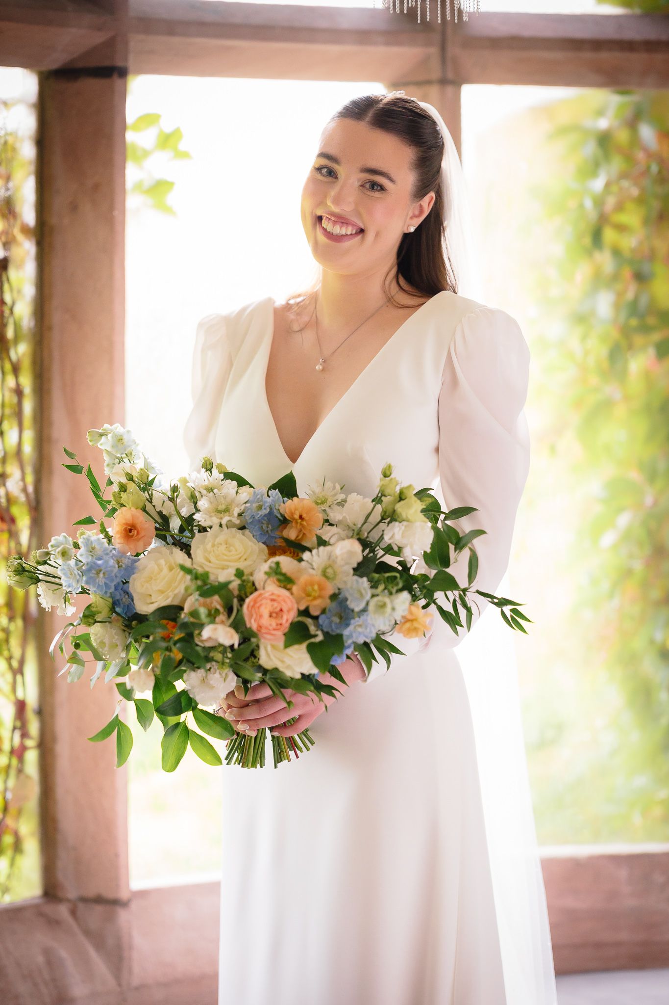 Beautiful spring bouquet with peach, blue and white flowers in a sunlit garden setting. Ellingham Hall