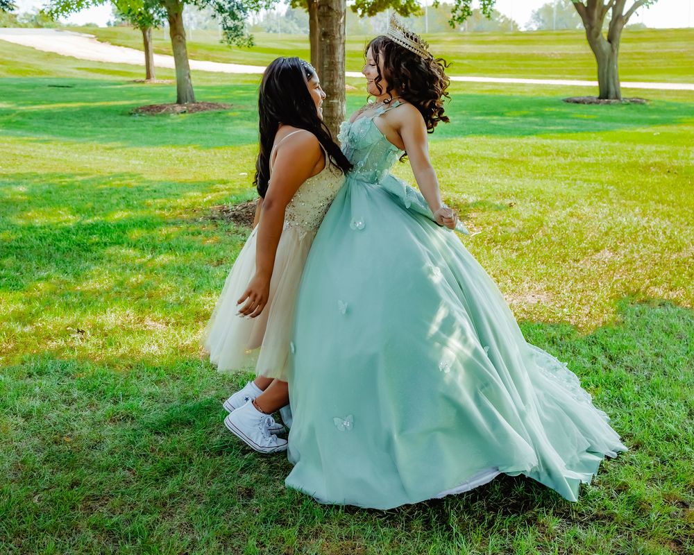 A person in a mint green gown sits on grass while a child in white leans in close during an outdoor photoshoot.