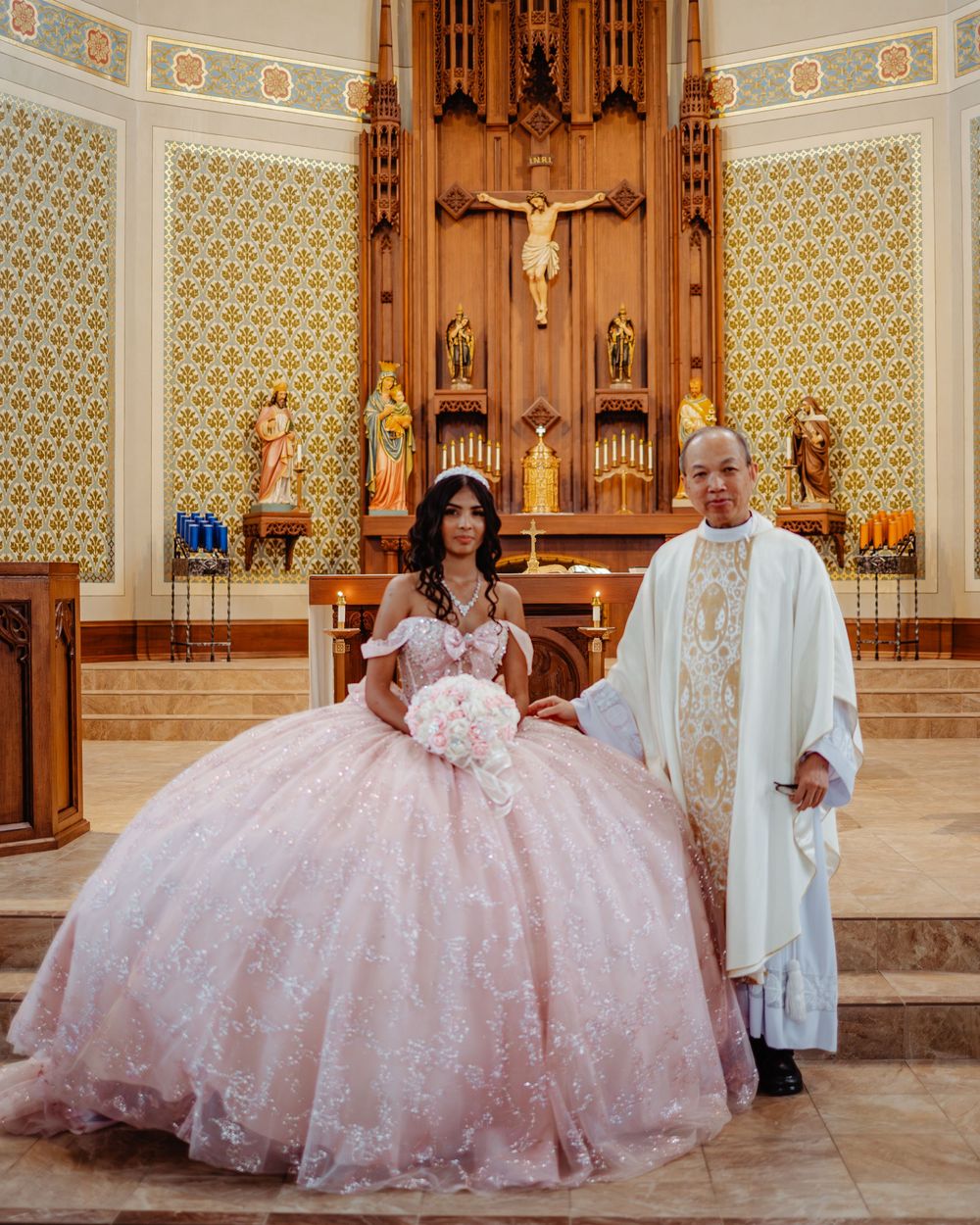 A stunning pink ball gown stands out against the ornate wooden altar and religious decor of a Catholic church interior.
