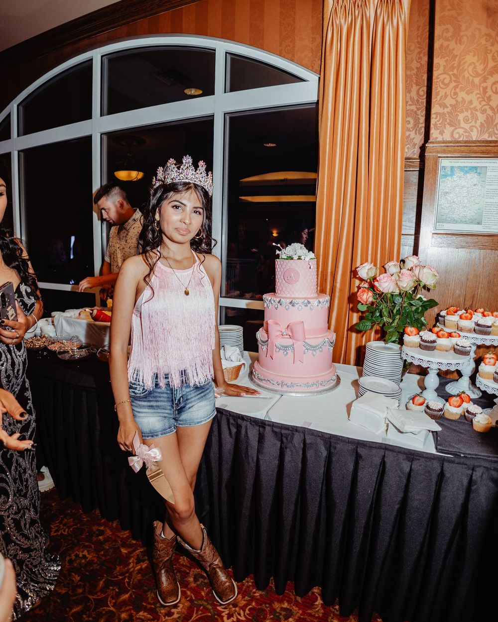 Pink tiered wedding cakes and desserts displayed on a black-draped table at an elegant reception venue.