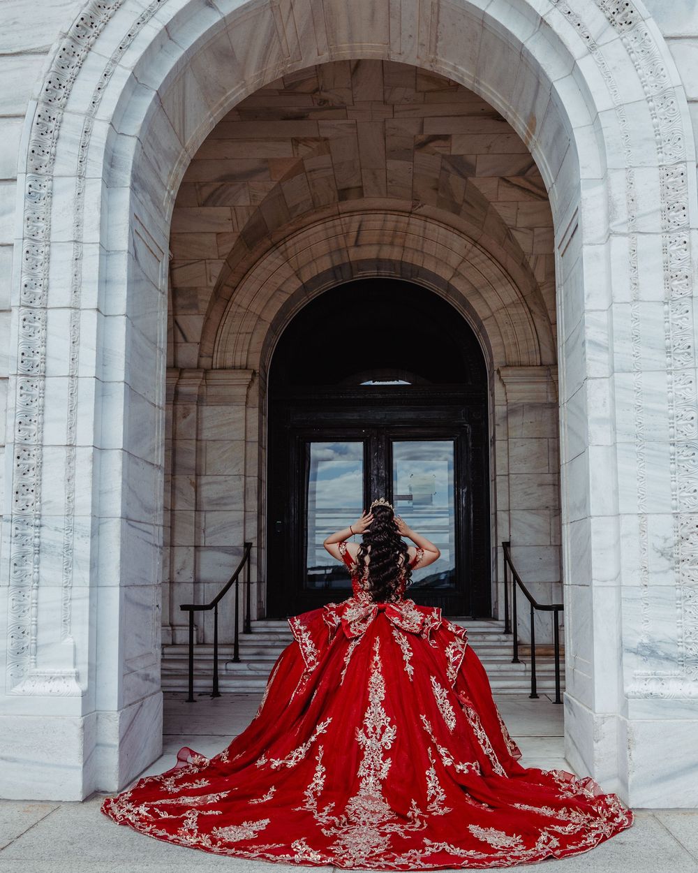 A dramatic red ballgown with intricate embroidery is photographed in a series of arched stone hallways.
