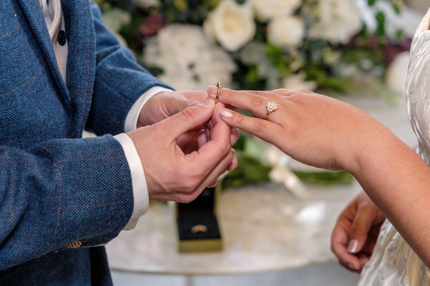 A couple exchanging wedding rings during an outdoor ceremony with greenery in the background.