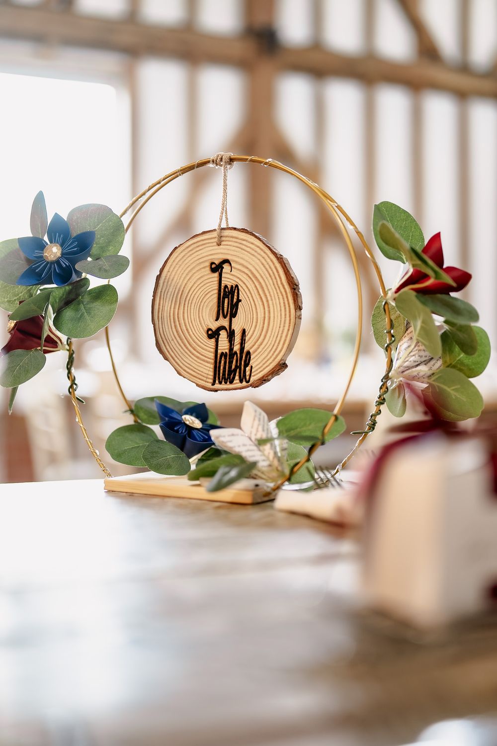 Rustic wooden wedding decor featuring a circular wood slice with text surrounded by blue and red artificial flowers.
