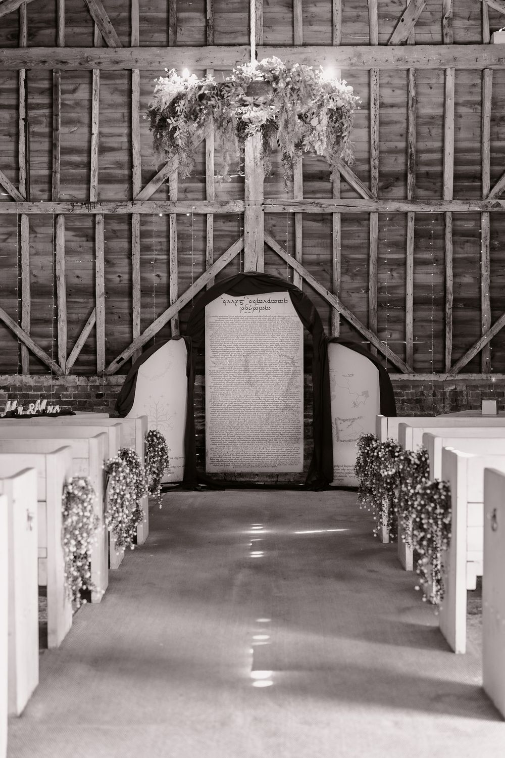 Rustic barn wedding chapel interior with wooden beams and floral decorations along the aisle.