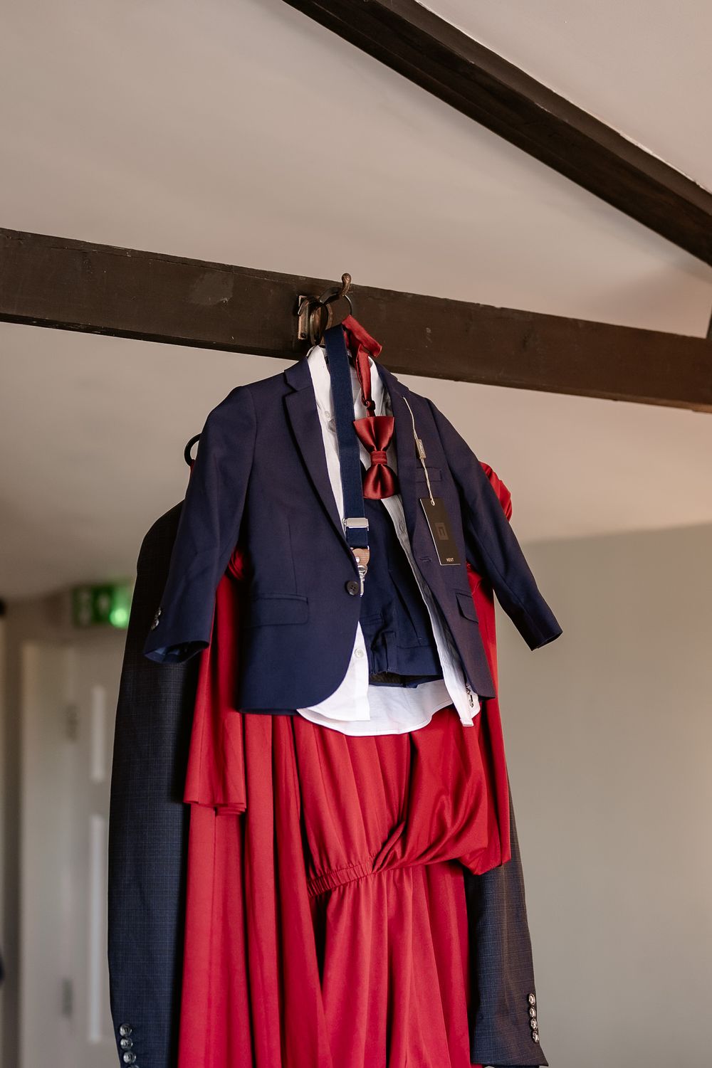 Navy blue suit jacket and red dress hanging from wooden ceiling beam.