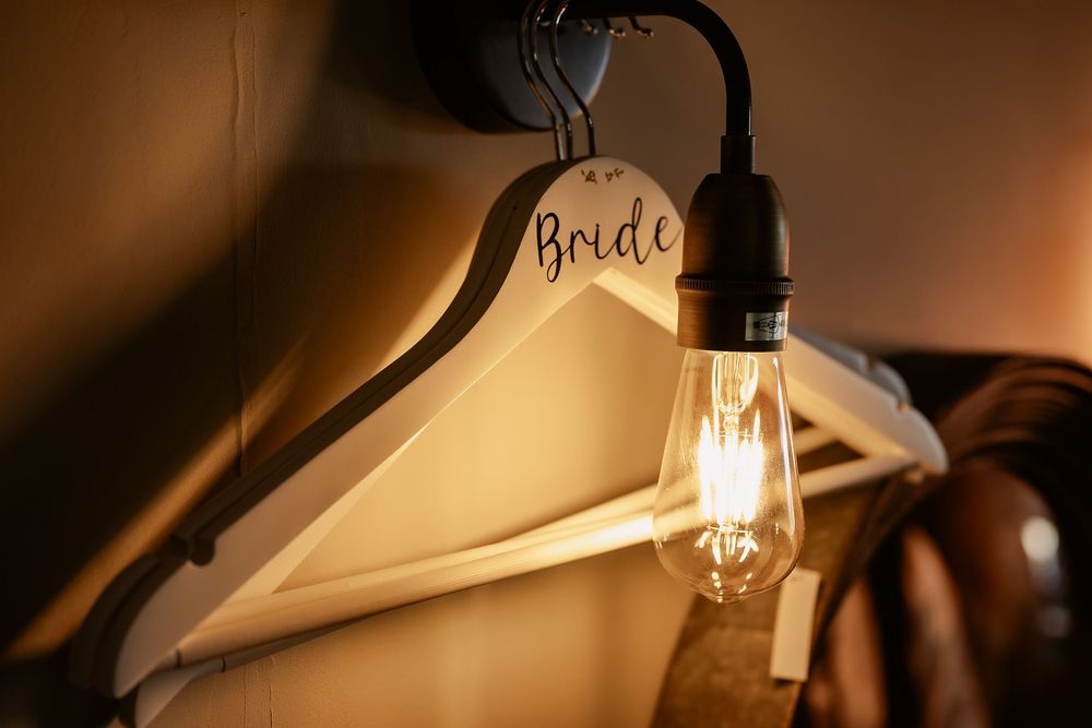 Illuminated light bulb hanging near white bridal dress hangers creating a warm, atmospheric glow.