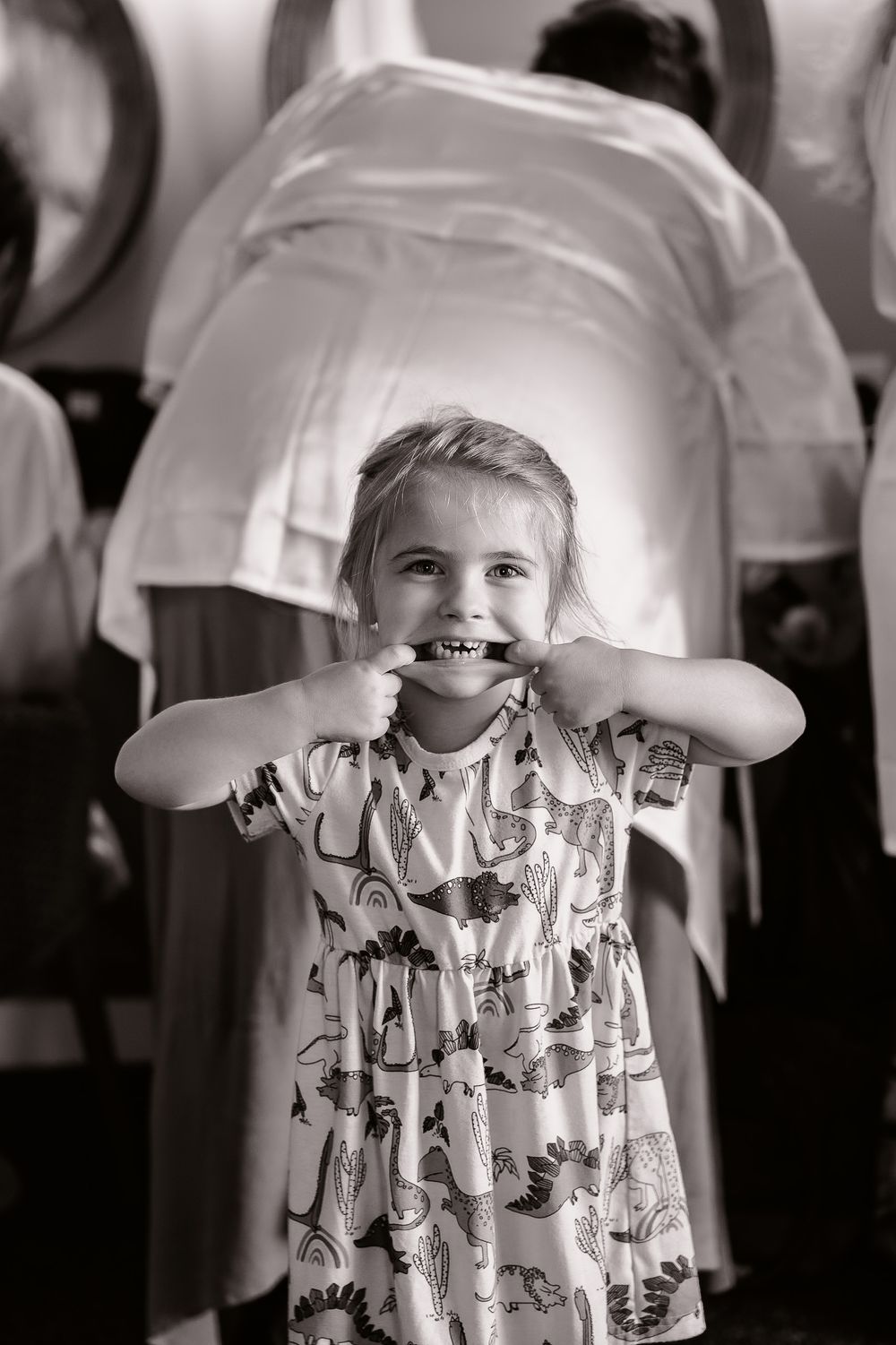 A young child making a silly face while wearing a patterned dress at a celebration.